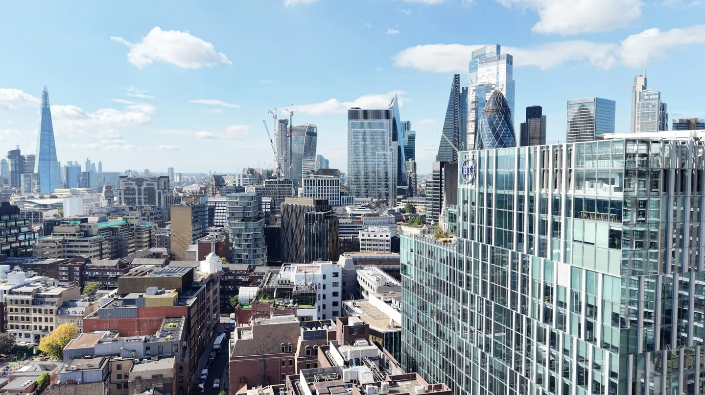 Aerial drone view across the City of London skyline, with the Gherkin, the Walkie-Talkie and the Shard above office rooftops