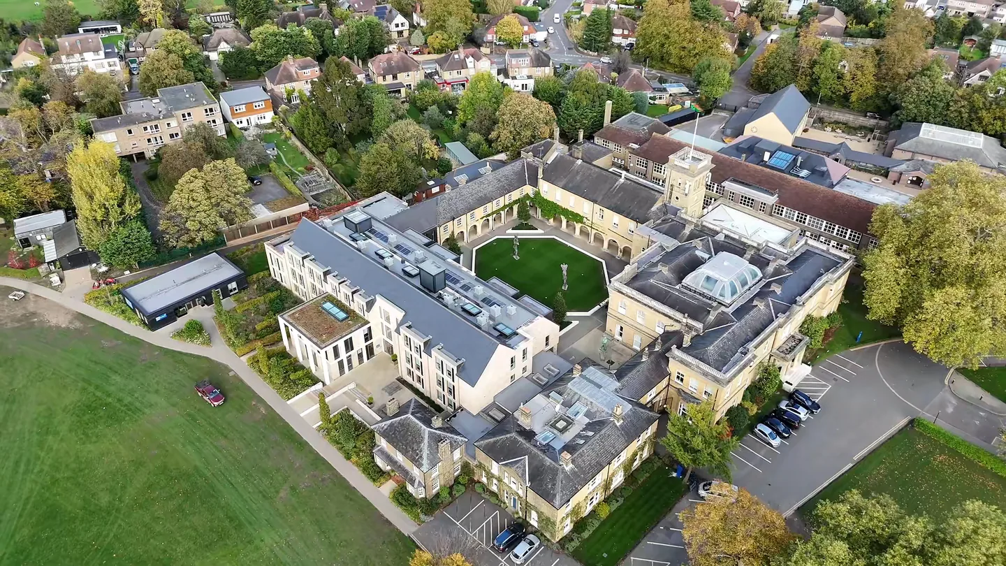 Aerial drone view of Eltham College, its Victorian slate roofs, clock tower and lantern around a central quadrangle, set among trees and playing fields