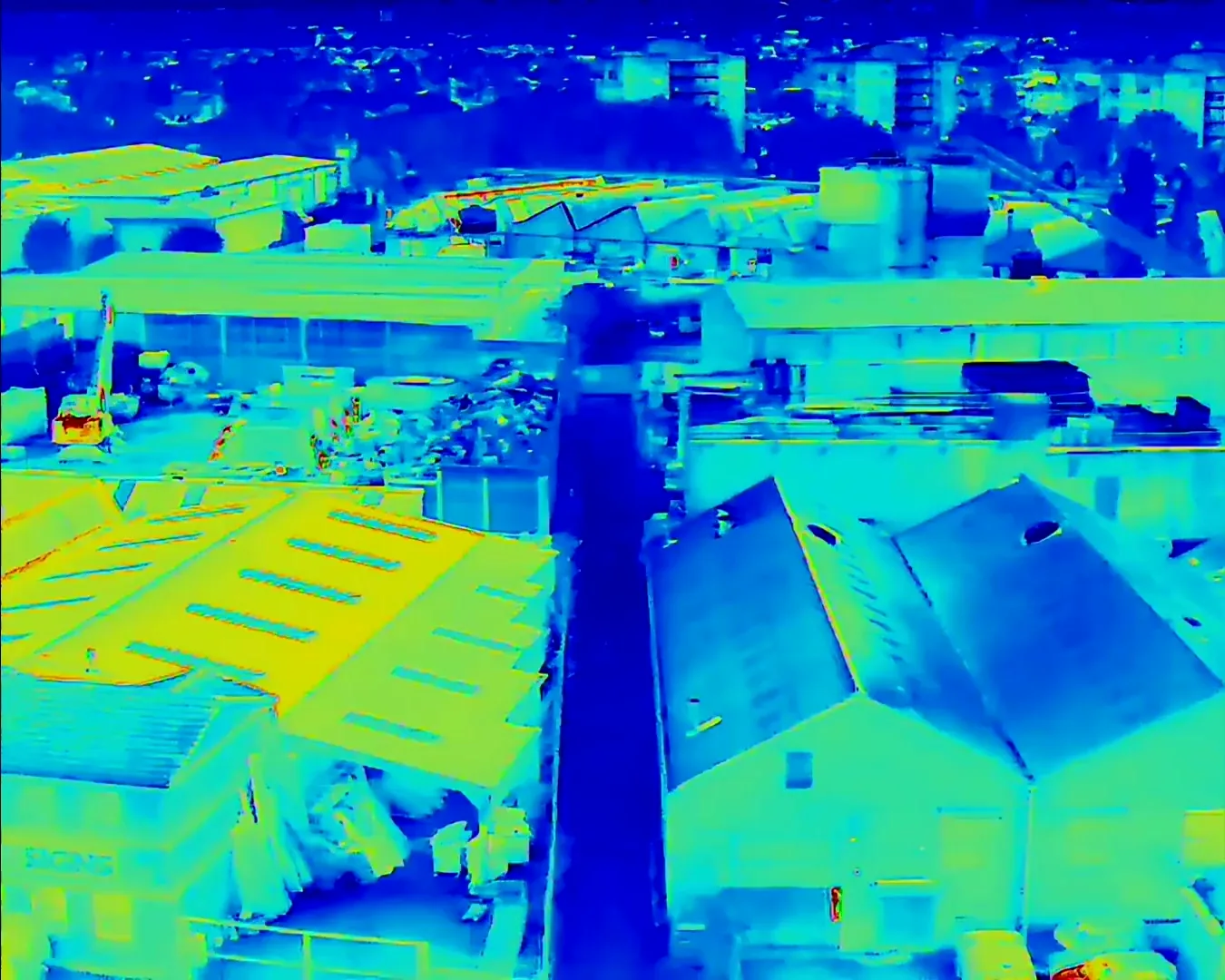 Thermal drone view over industrial and warehouse roofs, with warmer roof slopes in yellow against cooler blue buildings and streets
