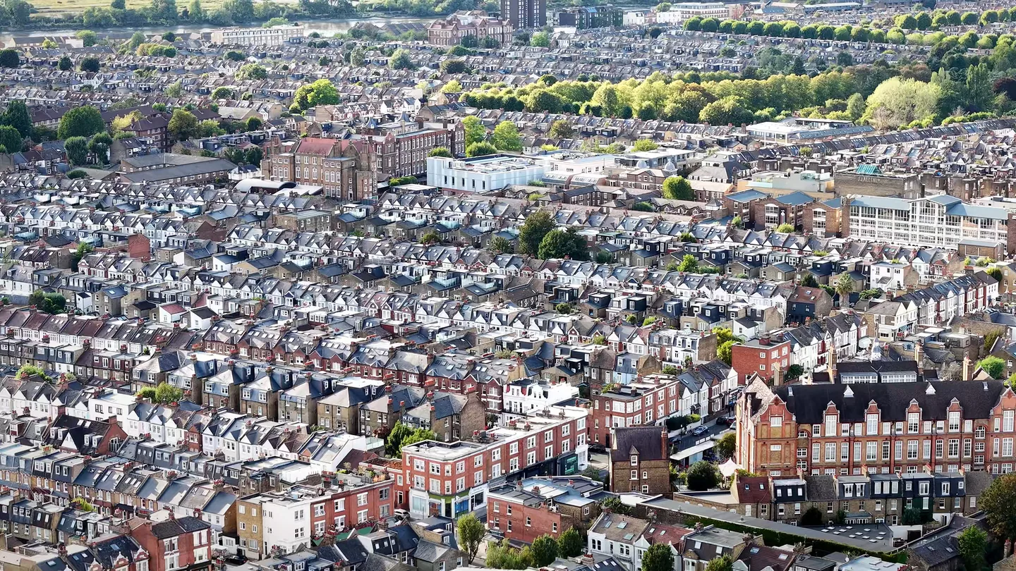 Drone view across rows of London Victorian terraced houses, with slate roofs, chimney stacks and red-brick mansion blocks