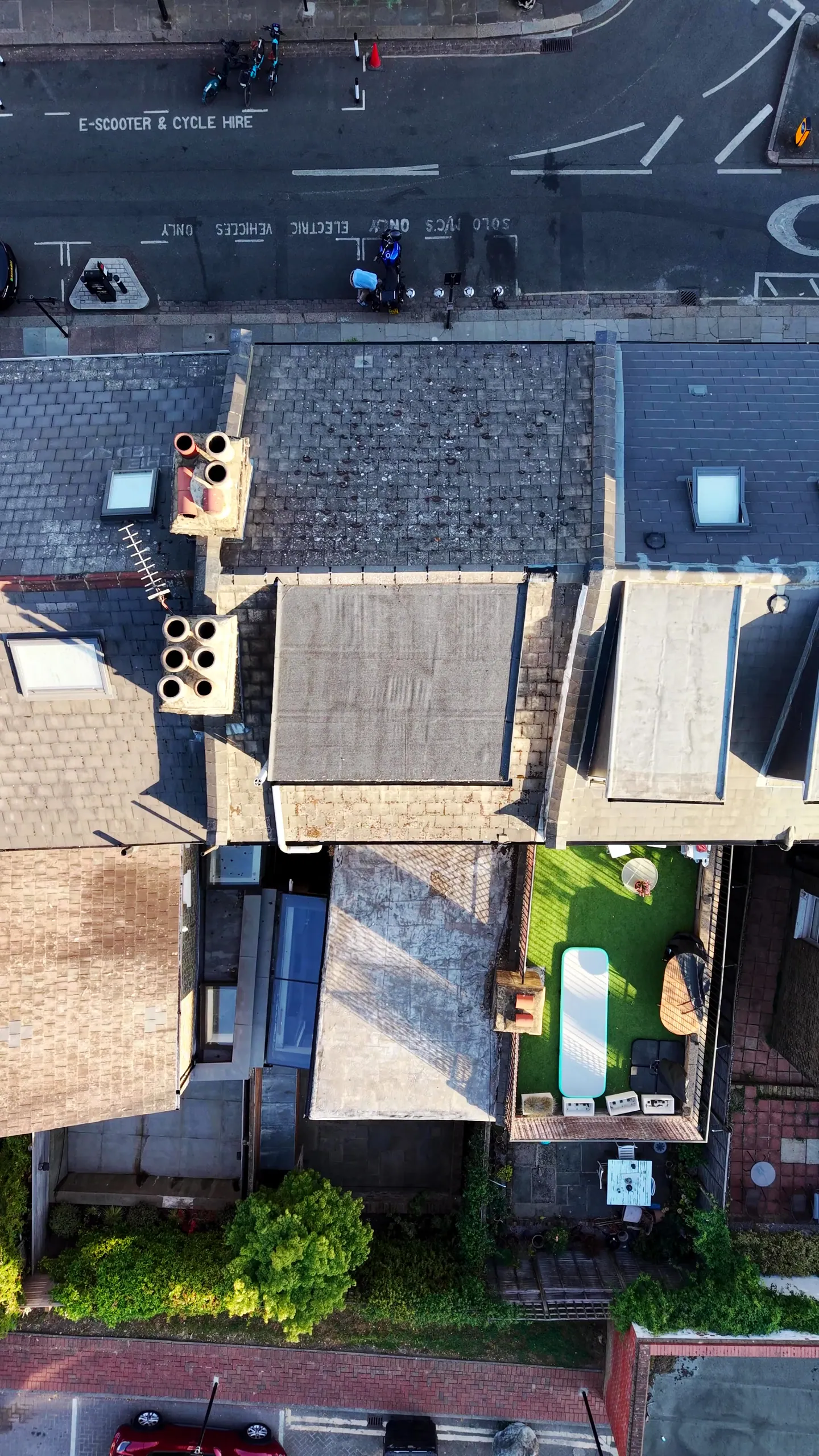 Top-down drone view of terraced house roofs in north-west London, showing slate slopes, a flat felt roof, chimney stacks and rear extensions
