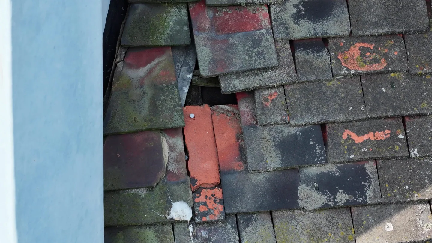 Close drone view of slipped and broken clay roof tiles, with an exposed gap to the timber batten beneath, moss and lichen