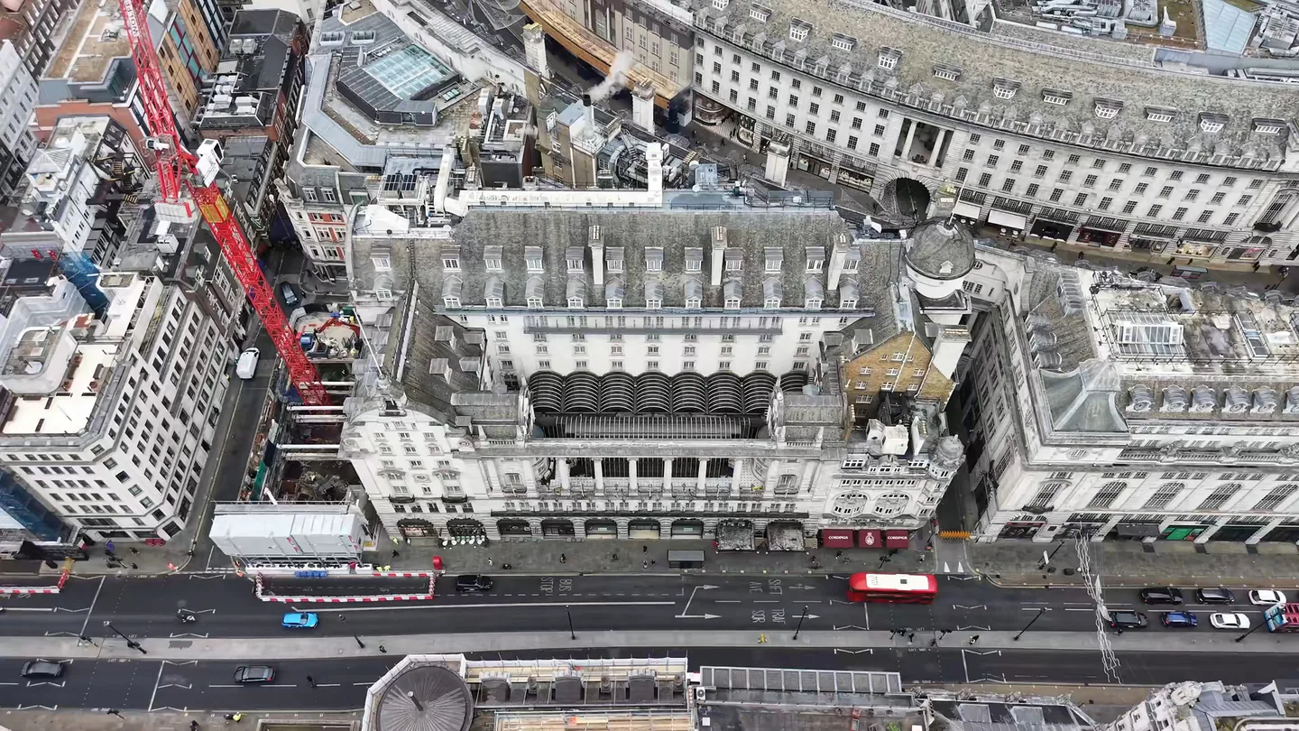 Drone view looking down on The Dilly hotel on Piccadilly, its mansard slate roof, dormers and copper-domed corner turret, with the street and a red bus below