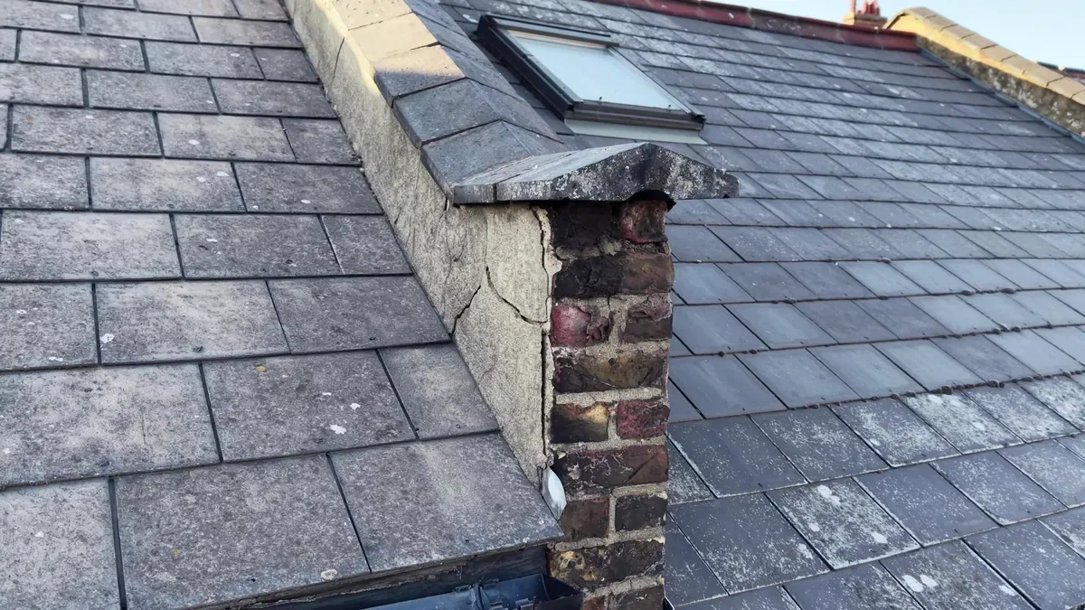 Slate roof with a rooflight and a party-wall parapet, where the render on the coping has cracked and exposed the brickwork
